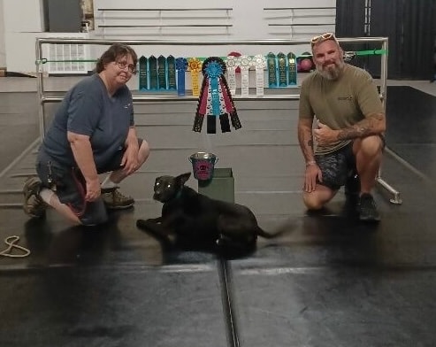 Two handlers posing with black lab and competition ribbons